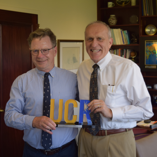 Two men pose holding sign featuring UCR letters