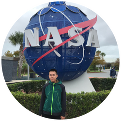photo of Jonathan Young, a UCR student with short dark hair, smiling at the camera and standing in front of a large NASA sign