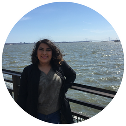 Photo of Imagen Soto Carbajal, a UCR student with dark hair who is smiling at the camera and standing by a railing near the ocean